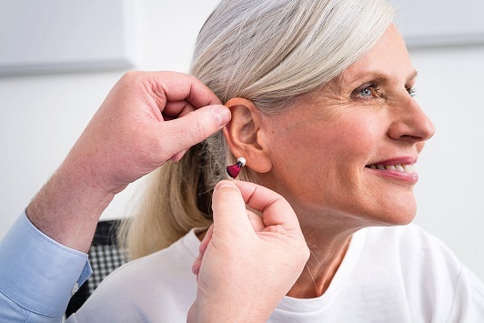 Ältere Frau bekommt ein modernes Hörgerät eingesetzt, Hörakustik und Hörhilfe.